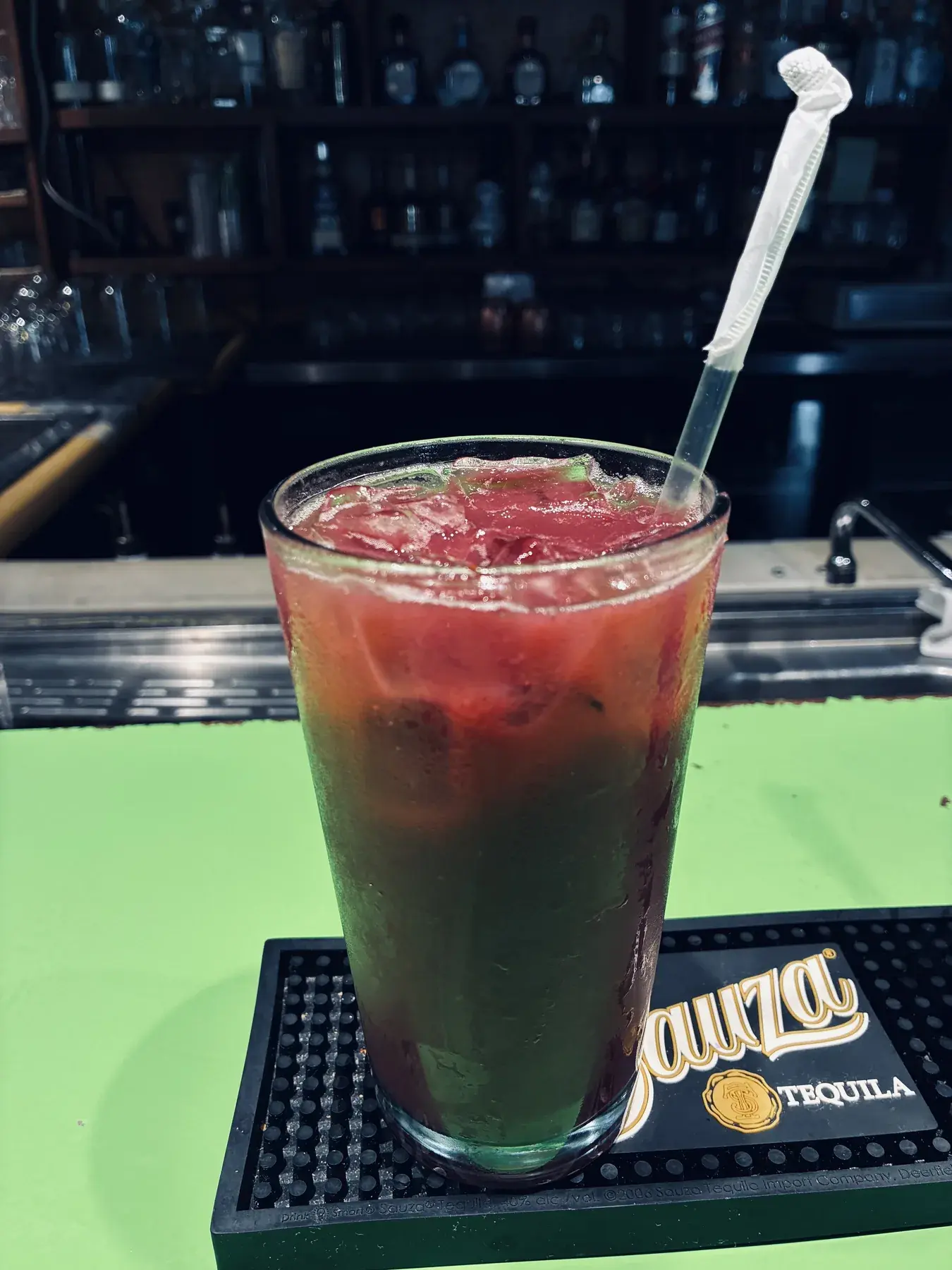 A ruby-red cocktail served with a straw and citrus garnish at the bar.