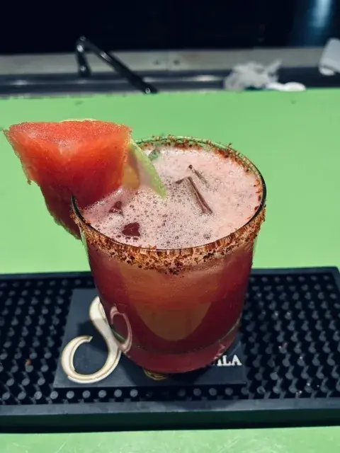 A bright red cocktail with fresh fruit garnish and a chile-salt rim.