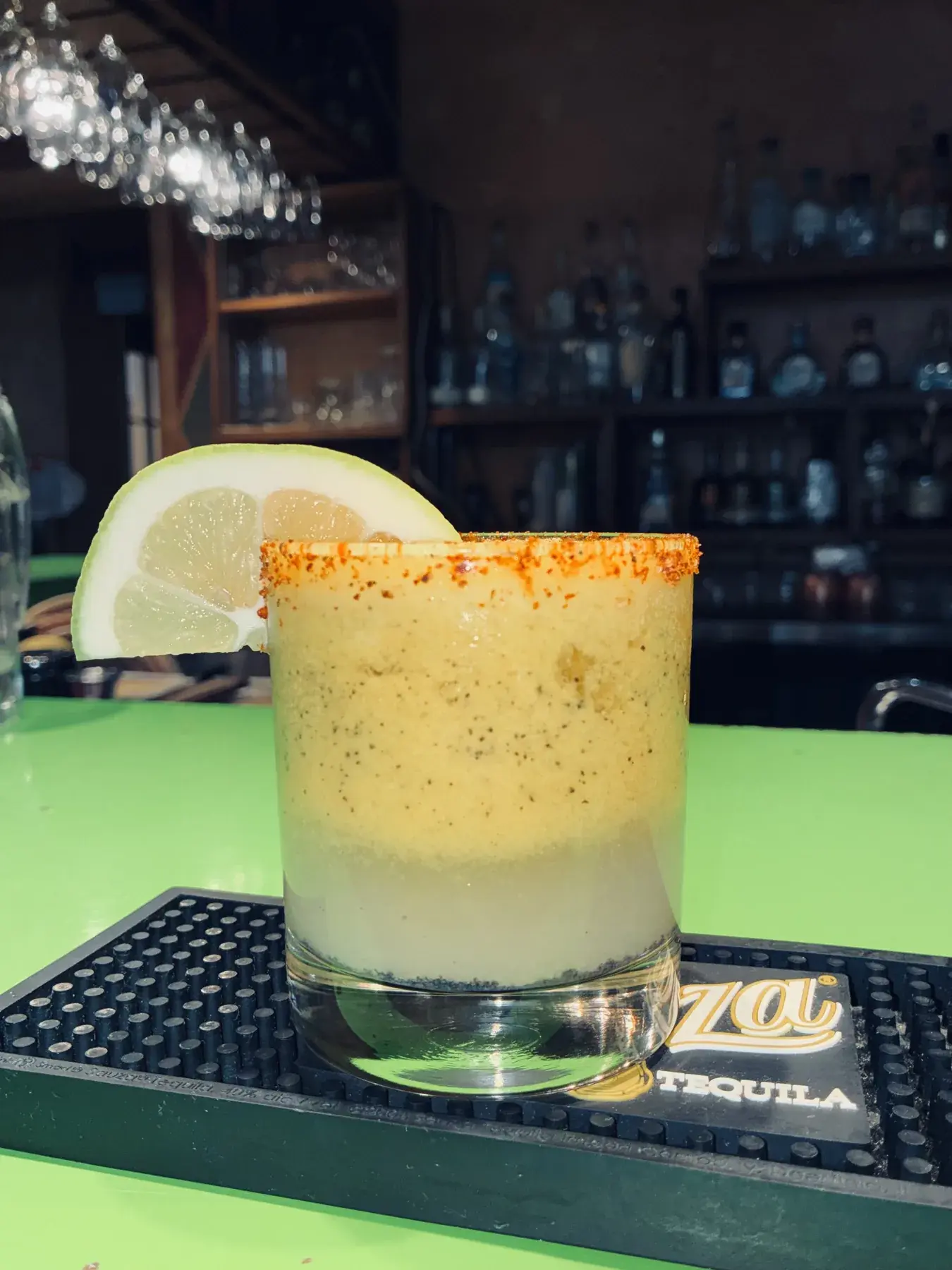 A creamy citrus cocktail with a chile-salt rim in front of the back bar.