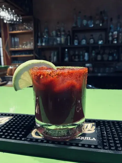 A deep-red cocktail with a lime garnish on the bar.